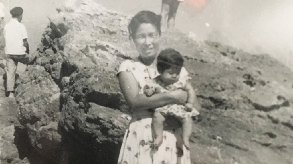 A black and white photograph of the founder's grandmother, holding the founder's mother as a baby. They're standing in front of a large rock.