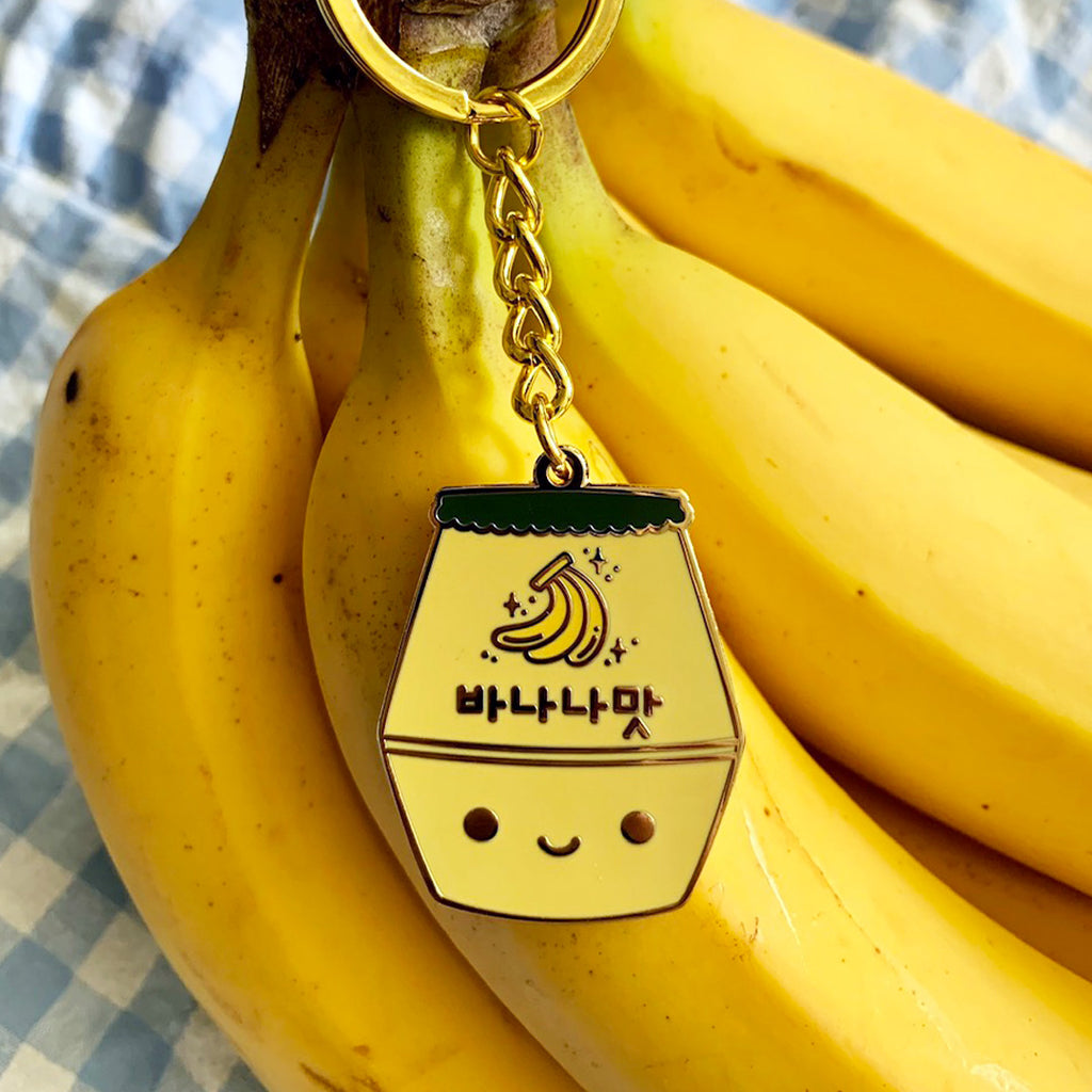 Banana milk keychain resting on top of a bunch of bananas