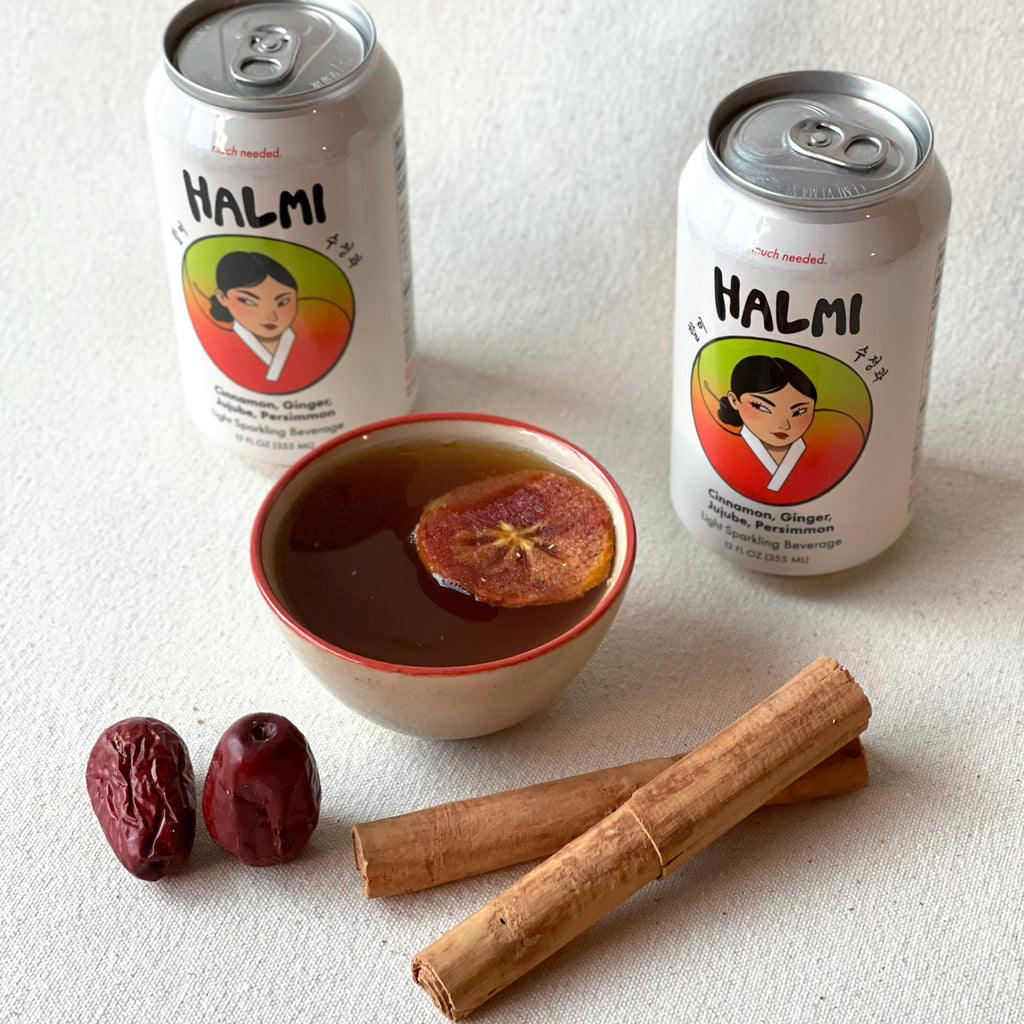 Two cans of Halmi next to a ceramic cup from Esther Plates, two cinnamon sticks and two dried jujubes
